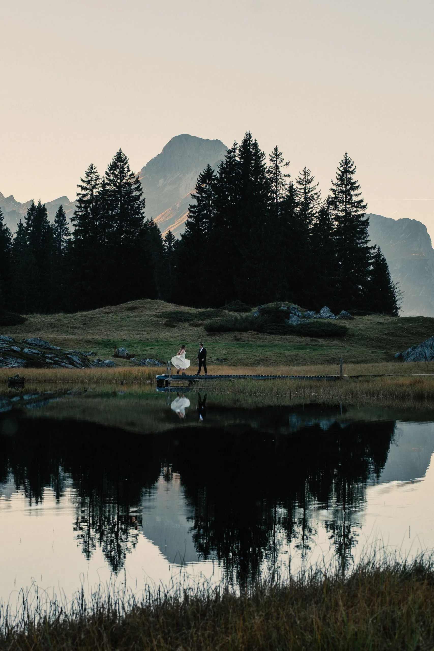 A couple reflected in a still alpine lake below a mountain peak in the Austrian Alps