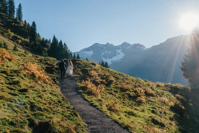 Ein Paar geht im Abendlicht einen goldenen Bergpfad entlang, allein in den Alpen