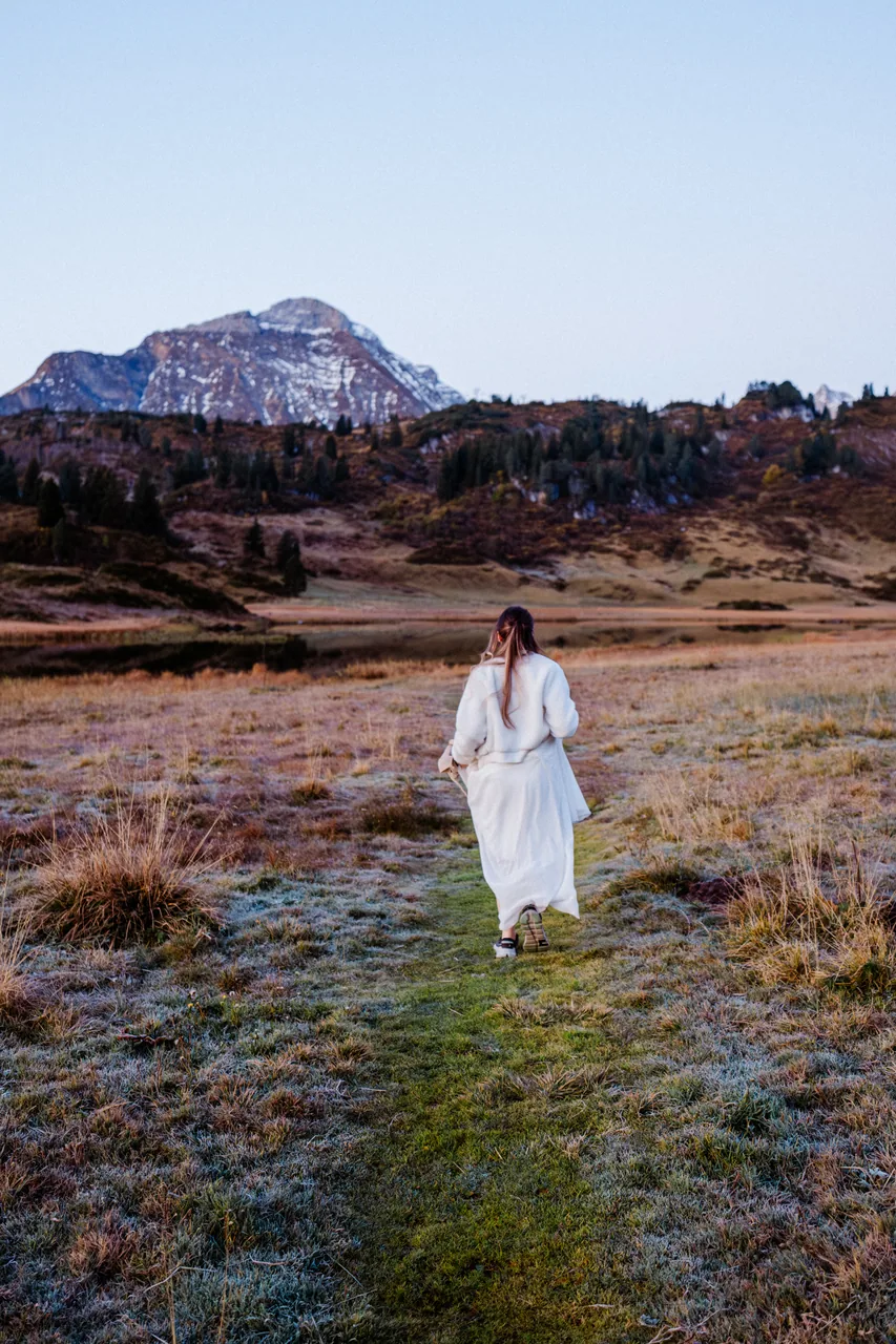 A bride walking a frosted alpine meadow toward a jagged peak at first light