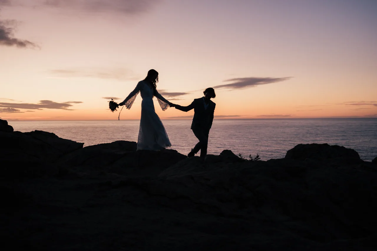 A couple alone on a clifftop ridge against a glowing evening sky