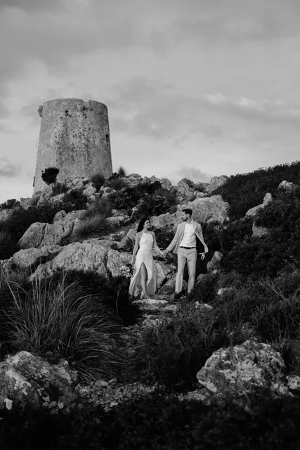 Couple walking below an old stone watchtower on the Mallorcan coast