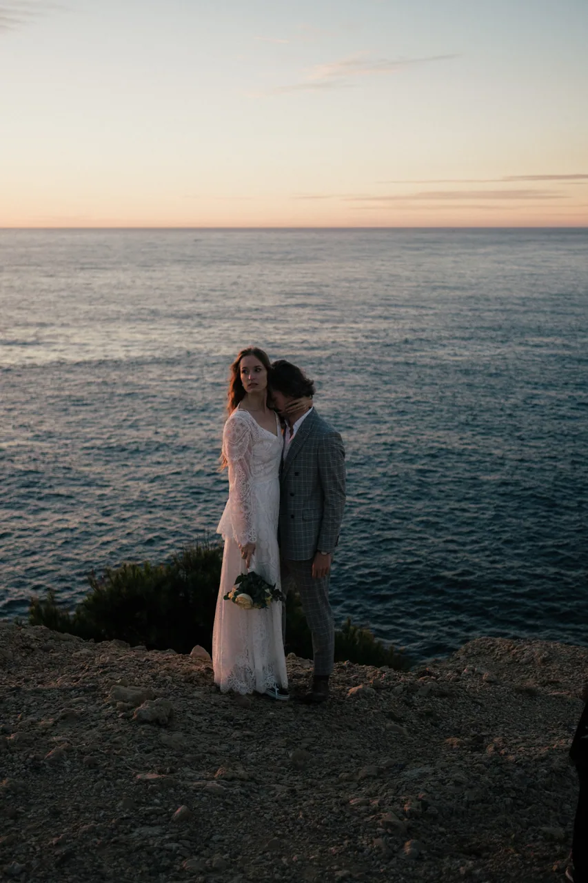 A couple holding each other on a clifftop above the sea at sunset