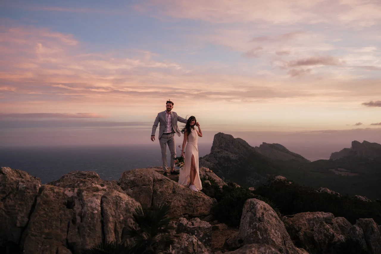 A couple on a rocky Mallorcan ridge under a pink evening sky